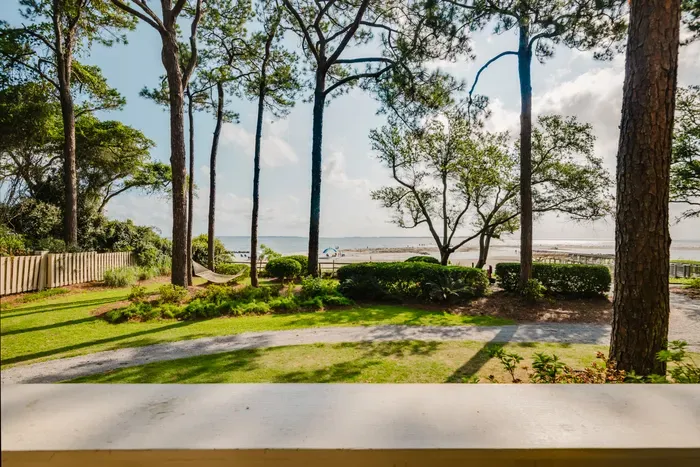 Serene beachfront view with shaded lawn, tall pines, and easy beach access