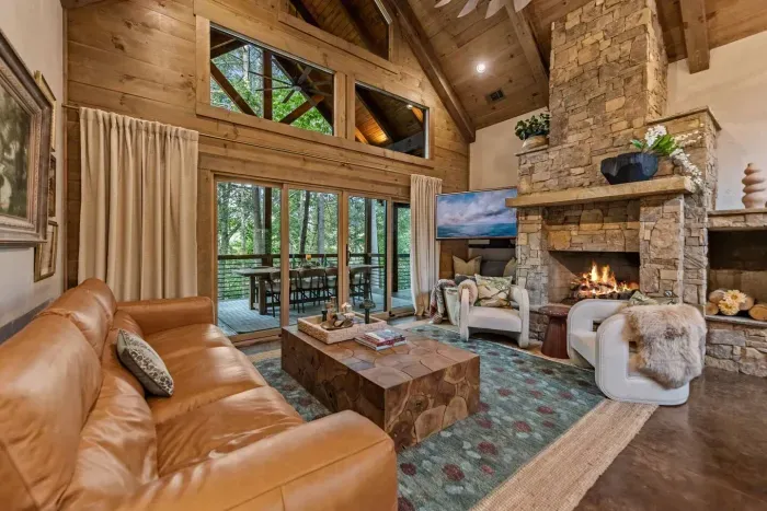 Gather in style around the soaring stone fireplace in this designer living room. Vaulted ceilings, floor-to-ceiling windows, and expansive deck create the perfect blend of rustic charm and modern comfort.