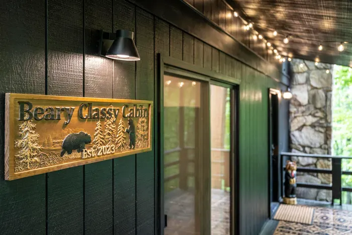 You've arrived. String lights on, sign lit, stone and green siding tucked into the woods — this is the walk up to the front door.