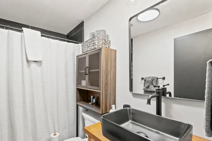 Black vessel sink on butcher block, framed mirror, waffle curtain. Clean and stocked.