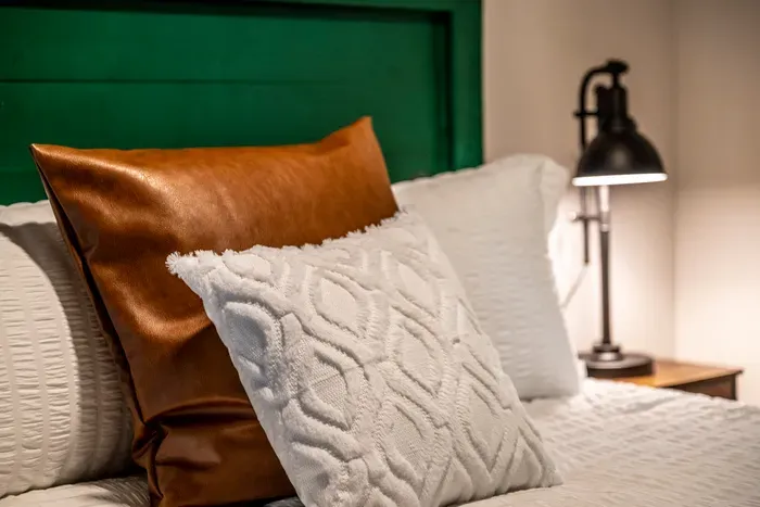 Emerald headboard, layered white bedding, caramel leather accent. Nightstand lamp within arm's reach for the readers.