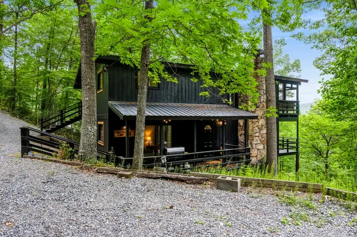 Covered wraparound porch with the grill already staged and string lights overhead. Rain doesn't cancel dinner here.