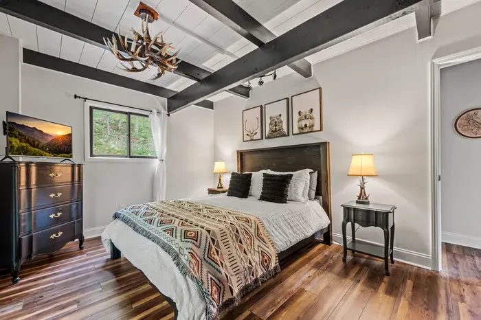 Stained wood headboard, woven throw, bear-deer-wolf trio on the wall. Smart TV and a window to the hillside.