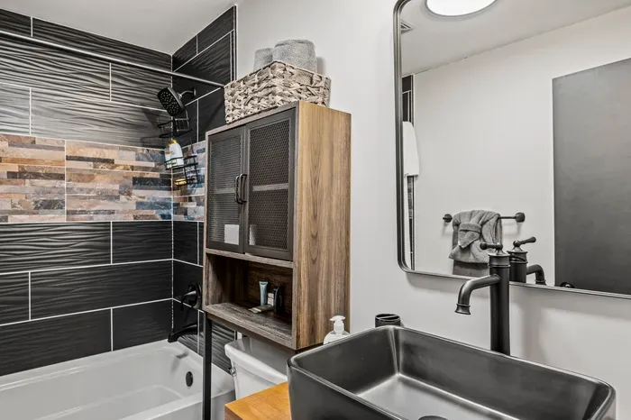 Full tub-shower with a stacked stone accent stripe. Towels, toiletries, and storage already set.