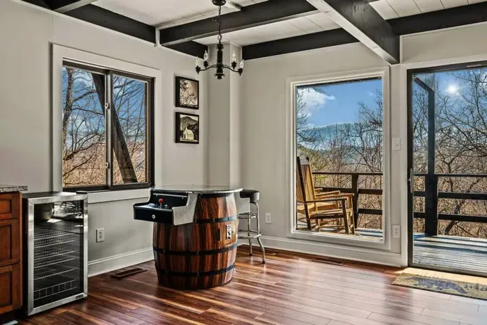 Barrel-style tabletop arcade next to the wet bar, with the deck and mountain view through the glass. Winter opens the view up completely.