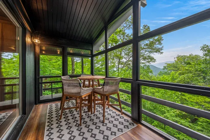 Screened balcony with dining table, treetop views, and a peaceful mountain backdrop
