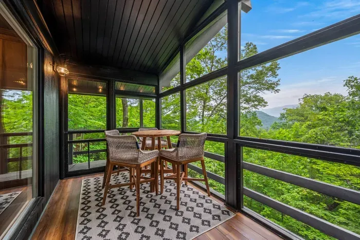 Screened porch with a high-top for four and a real Smokies ridgeline behind it. Bugs stay out, the view doesn't.