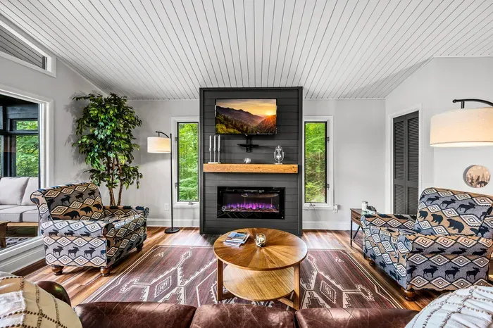 Live-edge mantel over an electric fireplace, flanked by windows on both sides. The upholstery went full Smokies and we regret nothing.