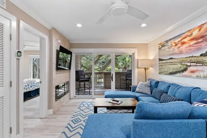 Balcony entrance view from living room, walls lined in shiplap, custom coastal artwork, Smart TV, Fireplace, and the ocean blue sectional.