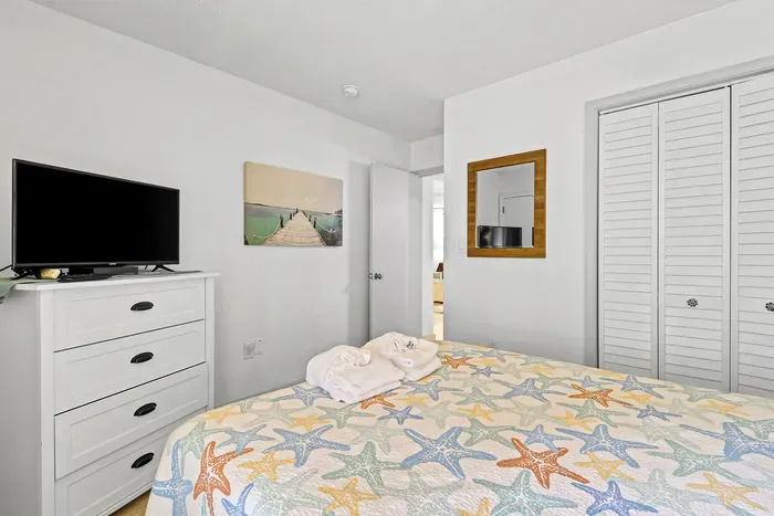 Bright coastal bedroom with TV, closet storage, and beach-inspired decor