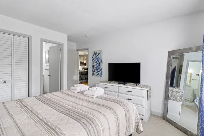 Bright, serene bedroom with TV, full-length mirror, and cozy coastal style
