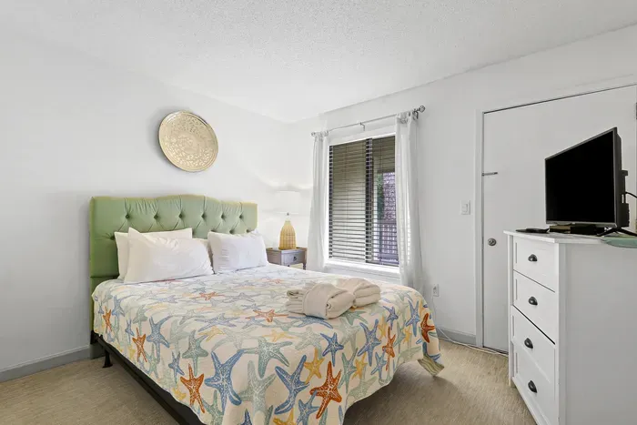 Bright coastal bedroom with TV, natural light, and a plush king bed