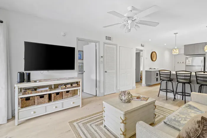 Bright open living room with large TV, breakfast bar, and airy coastal style