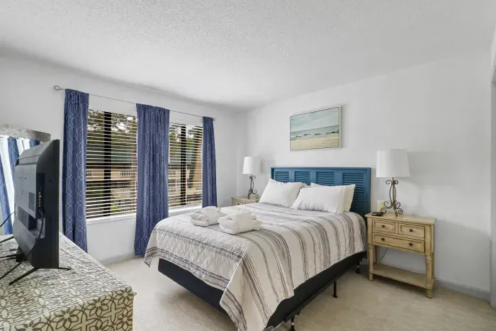 Bright coastal bedroom with TV, natural light, and a cozy guest-ready bed