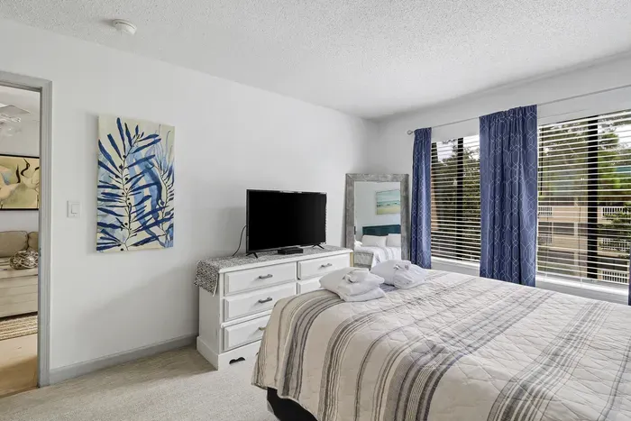Bright coastal-style bedroom with TV and large sun-filled corner windows