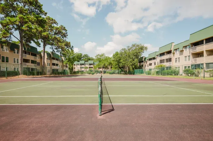 Sunny on-site tennis court surrounded by trees and resort-style condos