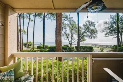 Covered balcony with serene water views, fan, and lush tree-lined setting