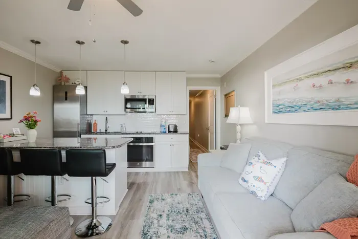 Open-concept living with a fully equipped kitchen — full-size fridge, oven, microwave, and cooktop. The hallway leads back to the bedroom and bath.