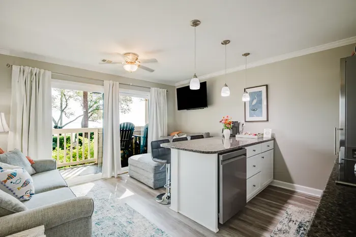 The whole villa opens toward the water. Sofa, bar seating, kitchen, and balcony all in one bright, connected space.