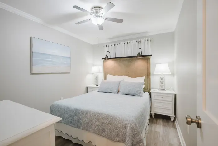 The bedroom sleeps two in comfort — plush queen bed, reading lights built into the headboard, ceiling fan, and blackout lined curtains for sleeping in.