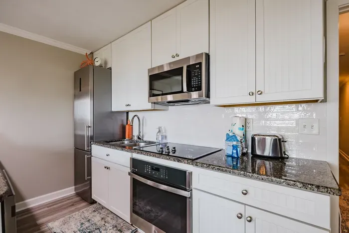 Fully stocked and ready to cook: full-size fridge, glass cooktop, oven, microwave, toaster, and cookware in the cabinets below.