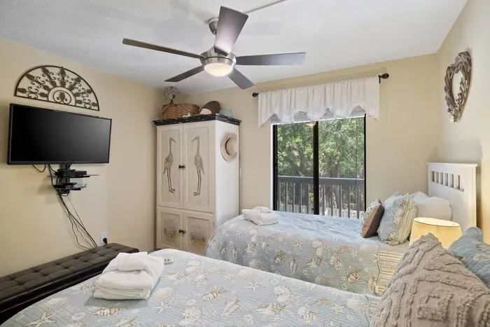A light beige-toned bedroom with two twin beds and SMART TV.