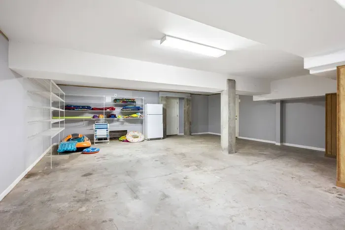 Ground-level storage with shelving stocked with pool floats and beach chairs, plus a second refrigerator for overflow.