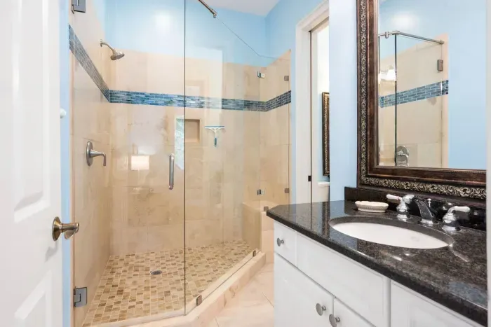 Oversized glass corner shower with a granite vanity alongside.