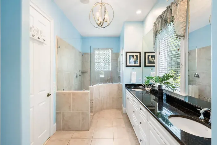 Glass-brick window, oversized tiled shower with dual heads, and a curved tub surround.