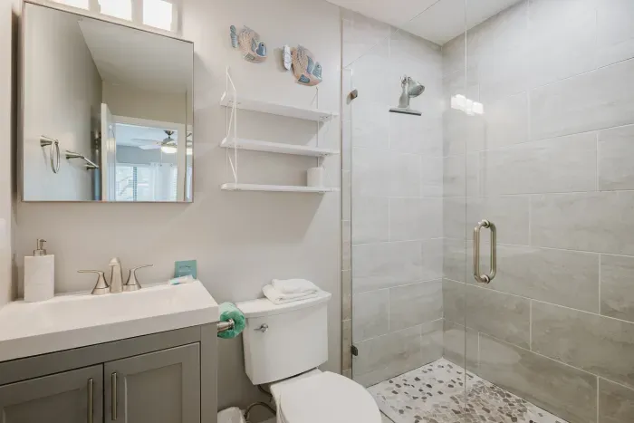 Renovated en suite with a glass walk-in shower, pebble-tile floor, and open shelving for your things. Towels stocked and ready.