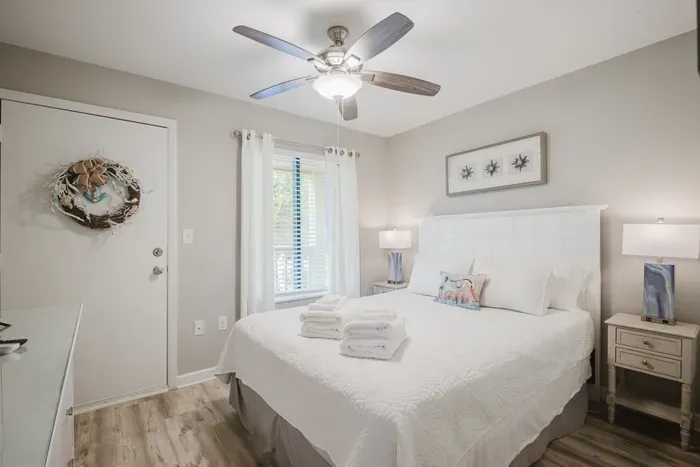 The second bedroom sleeps two comfortably dressed in crisp white linens, guest ready touches, and a bright window.