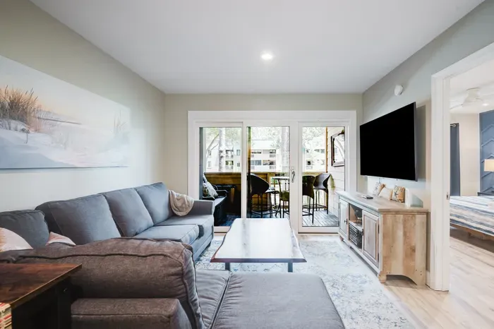 Bright living room with large sectional, TV, and private covered balcony