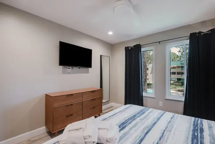 Bright modern bedroom with TV, dresser, and large sun-filled windows