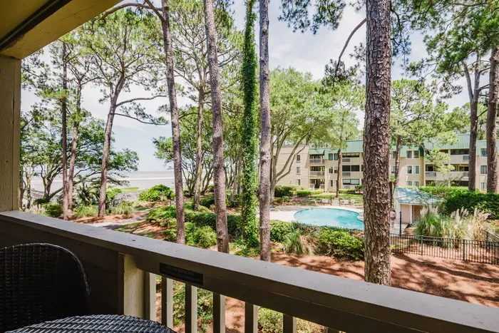 Covered balcony with pool views, towering pines, and a coastal backdrop