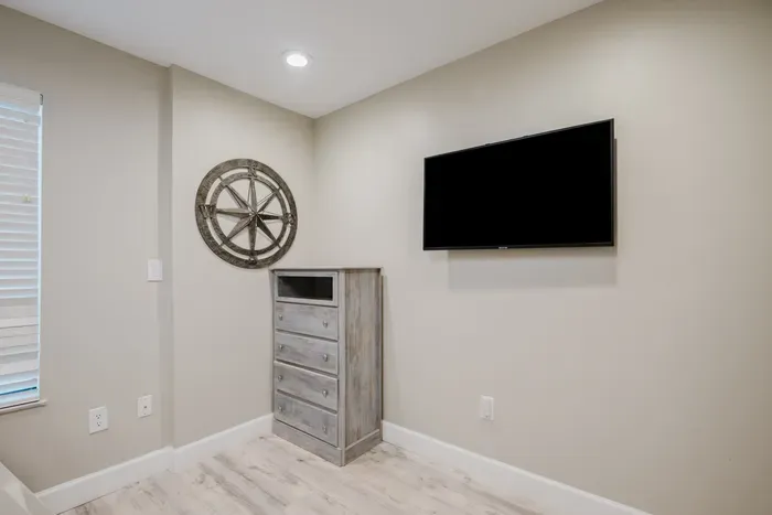 Wall-mounted TV and rustic dresser in a bright, modern guest space