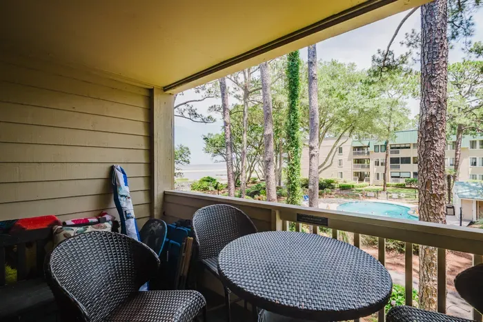 Covered balcony with pool views, towering pines, and a peek of the water