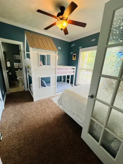 This playful bedroom includes a charming playhouse-style bunk bed and a cozy double bed set against a whimsical cloud-painted wall. Soft lighting and cozy bedding make it a fun and relaxing space for kids or the young at heart. Taken July 2025.