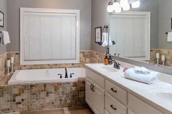 A luxurious master bathroom features a wide dual-sink vanity with ample counter space, warm lighting, and elegant fixtures. A large mirror spans the wall, while soft tones and clean lines create a spa-like retreat for relaxation and comfort.