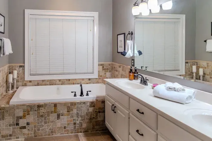 A luxurious master bathroom features a wide dual-sink vanity with ample counter space, warm lighting, and elegant fixtures. A large mirror spans the wall, while soft tones and clean lines create a spa-like retreat for relaxation and comfort.