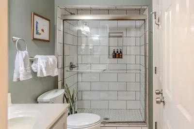 A beautifully tiled bathroom features a walk-in shower with elegant stone-look tiles, a frameless glass door, and modern black fixtures. Clean lines, warm tones, and sleek design elements create a refined, spa-like atmosphere.