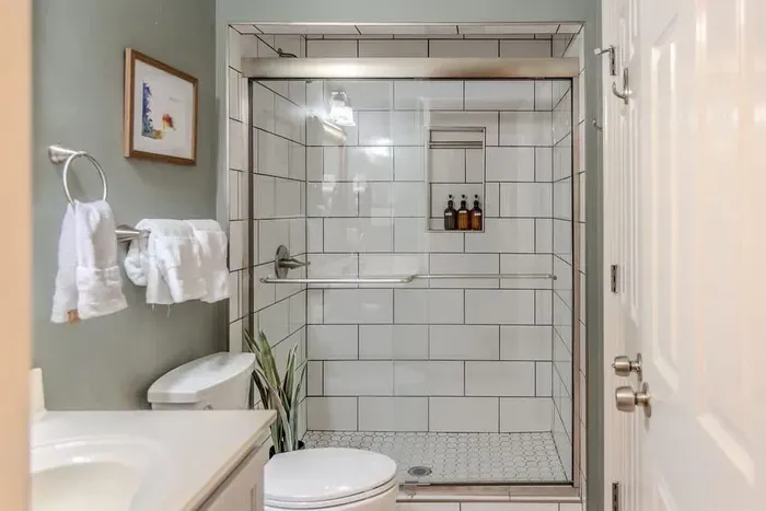 A beautifully tiled bathroom features a walk-in shower with elegant stone-look tiles, a frameless glass door, and modern black fixtures. Clean lines, warm tones, and sleek design elements create a refined, spa-like atmosphere.