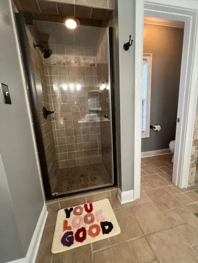 A sleek, modern shower features frameless glass doors, polished tile walls, and a built-in shelves for added comfort. Elegant fixtures and neutral tones create a spa-inspired atmosphere, perfect for unwinding in the master suite.
