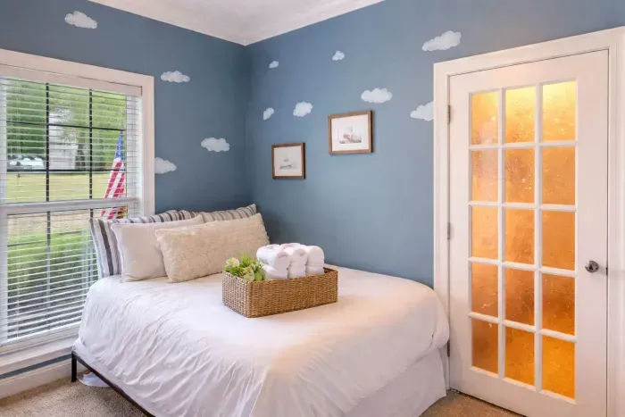 A whimsical bedroom features a playhouse-style bunk bed with a small ladder and window cutouts, perfect for imaginative play. Nearby, a double bed rests against a dreamy clouds, combining cozy comfort with playful charm for a family-friendly retreat.