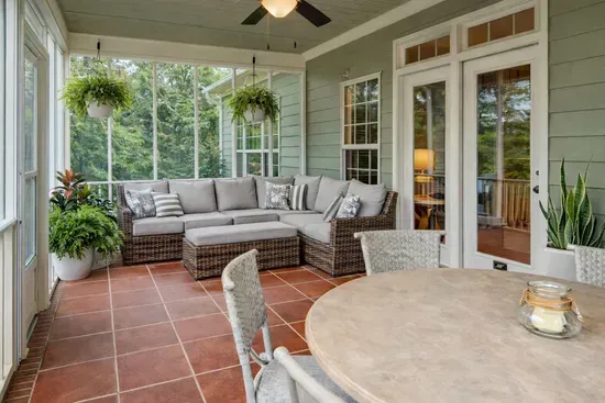 A cozy cushioned wicker couch with soft pillows invites relaxation on this serene back porch, which overlooks a tranquil lake and a charming water feature—offering peaceful views and the soothing sounds of nature.