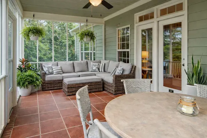 A cozy cushioned wicker couch with soft pillows invites relaxation on this serene back porch, which overlooks a tranquil lake and a charming water feature—offering peaceful views and the soothing sounds of nature.