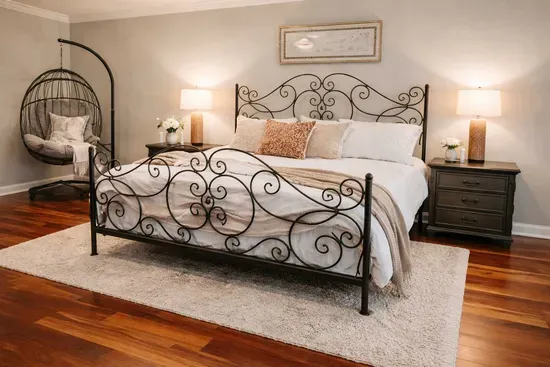 Elegant king bedroom with a beautifully crafted iron bed, plush linens, and soft bedside lighting. The space features rich hardwood floors and a cozy sitting corner—perfect for relaxing after a day of travel or exploring the area.

*Rug removed 