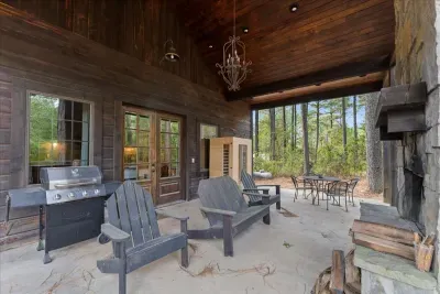 Covered outdoor space with a fireplace, grill, and dining area surrounded by nature.