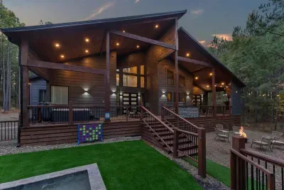 Spacious modern cabin exterior featuring large covered decks warm lighting and inviting outdoor seating surrounded by tall pine trees