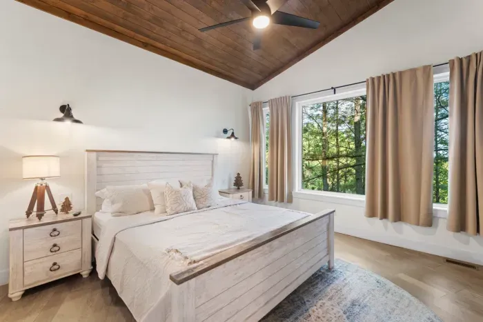 Relax in this gorgeous bedroom boasting a warm wood-paneled ceiling and large windows framing lush forest views.
