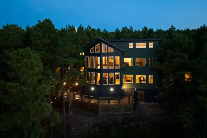 Bask in the cozy glow of our expansive windows lighting up the evening woods.